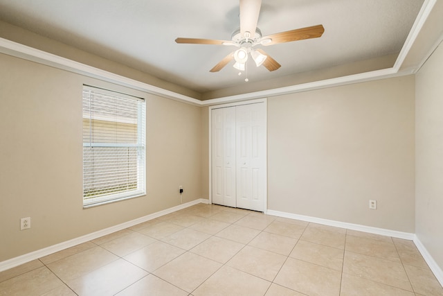 unfurnished bedroom with ceiling fan, a raised ceiling, light tile patterned floors, and a closet