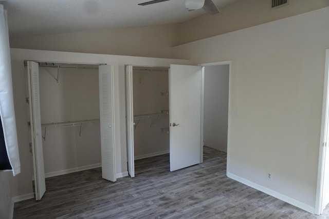 unfurnished bedroom featuring ceiling fan, vaulted ceiling, wood-type flooring, and two closets