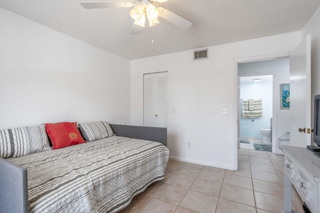 tiled bedroom with ceiling fan, a textured ceiling, connected bathroom, and a closet