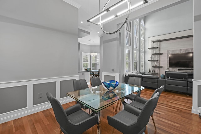 dining space with wood-type flooring, a towering ceiling, crown molding, and a notable chandelier