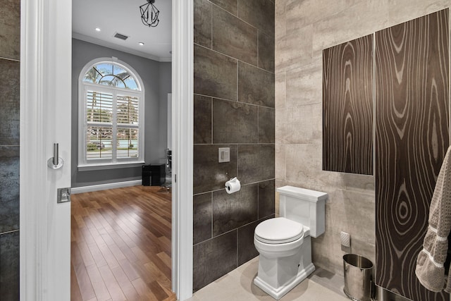 bathroom with hardwood / wood-style flooring, toilet, ornamental molding, and tile walls