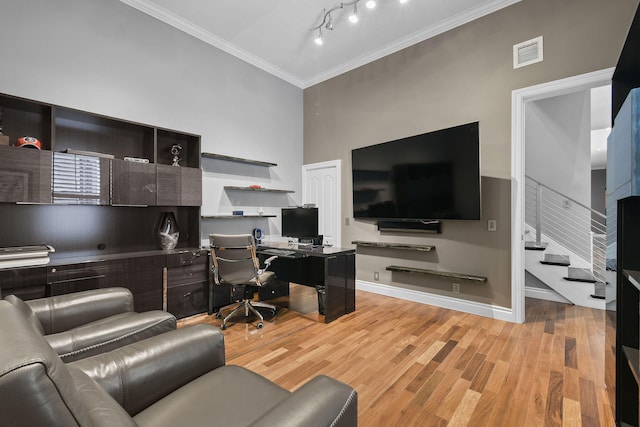 home office with a high ceiling, light hardwood / wood-style floors, and ornamental molding