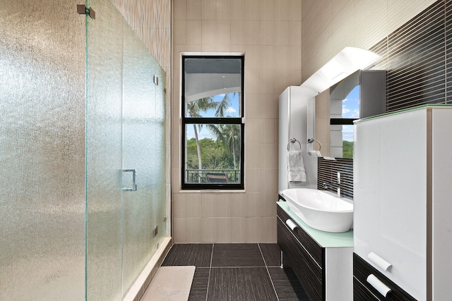 bathroom featuring tile patterned floors, vanity, a shower with shower door, and tile walls