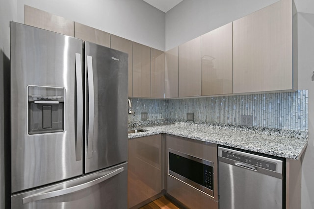 kitchen with light stone countertops, sink, stainless steel appliances, backsplash, and hardwood / wood-style flooring