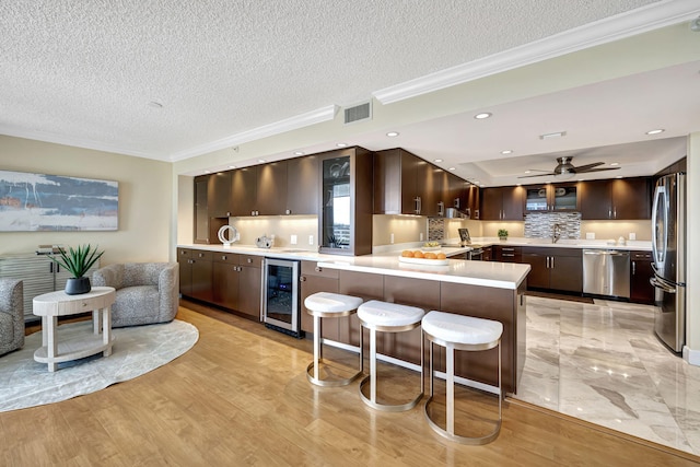 kitchen with beverage cooler, kitchen peninsula, light hardwood / wood-style floors, a breakfast bar, and appliances with stainless steel finishes