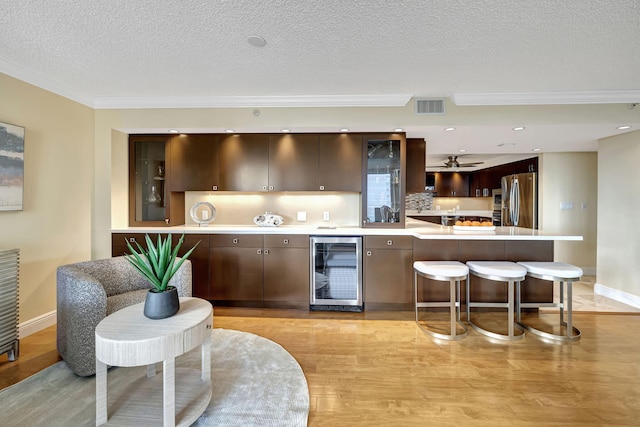 kitchen featuring ceiling fan, wine cooler, light hardwood / wood-style floors, stainless steel refrigerator, and dark brown cabinetry