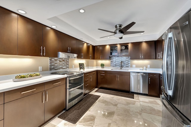 kitchen with dark brown cabinets, stainless steel appliances, a tray ceiling, ceiling fan, and sink