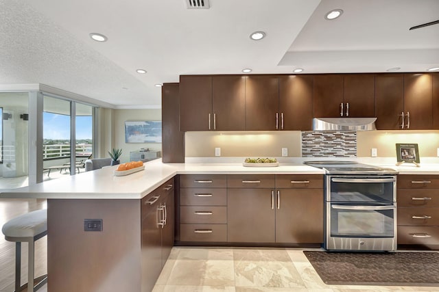 kitchen featuring kitchen peninsula, stainless steel range with electric stovetop, a kitchen bar, and dark brown cabinetry