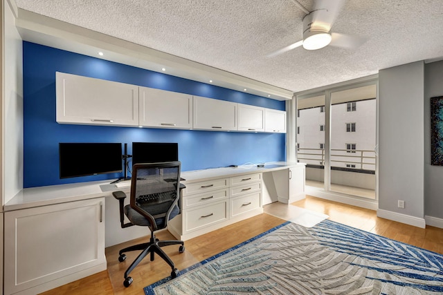 office space with ceiling fan, light hardwood / wood-style flooring, built in desk, and a textured ceiling