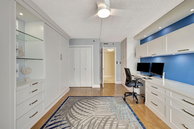 office featuring ceiling fan, built in desk, light hardwood / wood-style floors, and a textured ceiling