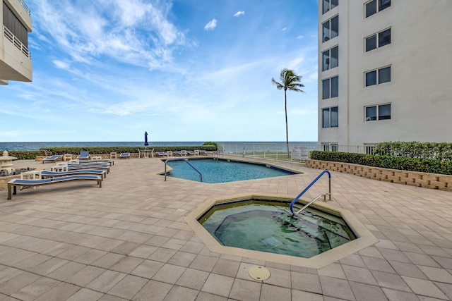 view of swimming pool featuring a patio area, a water view, and a hot tub