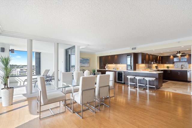 dining room with beverage cooler, ornamental molding, a textured ceiling, ceiling fan, and light wood-type flooring