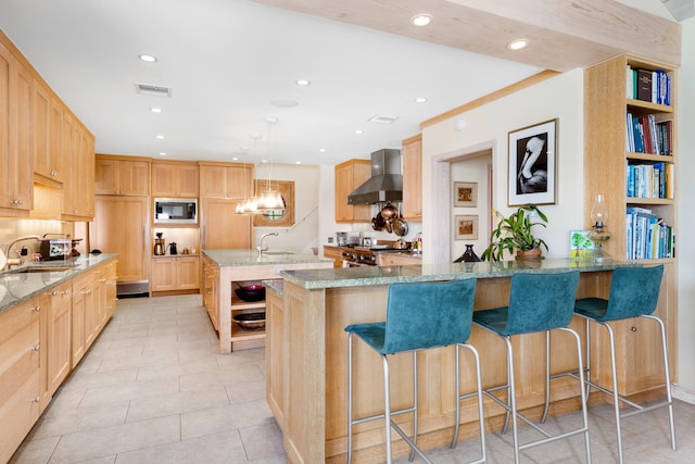 kitchen featuring hanging light fixtures, built in microwave, wall chimney range hood, kitchen peninsula, and light stone counters