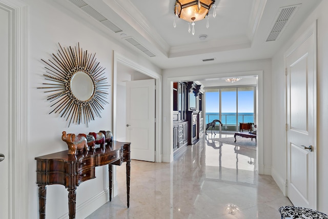 hall with ornamental molding, a water view, and a tray ceiling