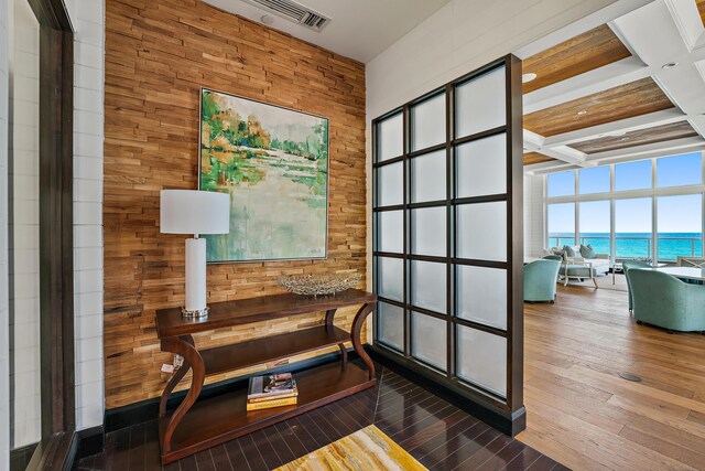 sitting room with dark hardwood / wood-style floors, wood walls, coffered ceiling, a water view, and beam ceiling