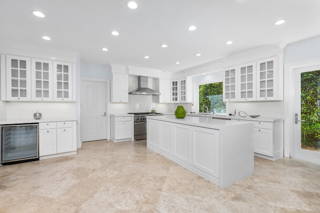 kitchen featuring high end stove, white cabinetry, wall chimney exhaust hood, and beverage cooler