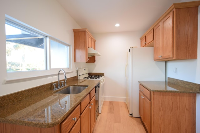 kitchen featuring sink, stainless steel range with gas cooktop, light hardwood / wood-style flooring, white fridge, and dark stone counters