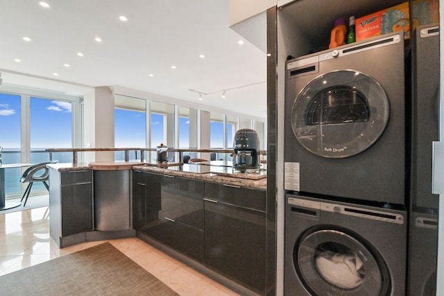 washroom with stacked washer / drying machine, a wealth of natural light, light tile patterned floors, and a water view