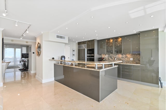 kitchen featuring light stone countertops, tasteful backsplash, crown molding, a spacious island, and appliances with stainless steel finishes