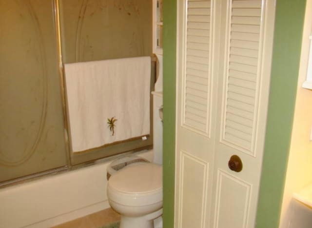 bathroom with bath / shower combo with glass door and toilet