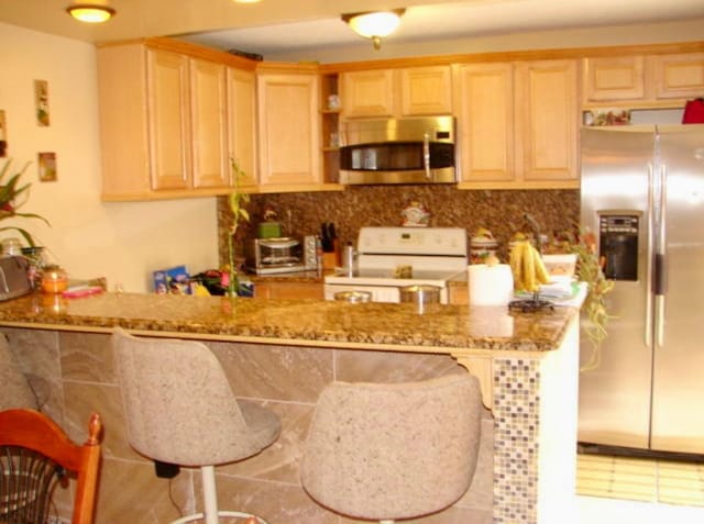 kitchen featuring a kitchen breakfast bar, kitchen peninsula, light stone countertops, and appliances with stainless steel finishes