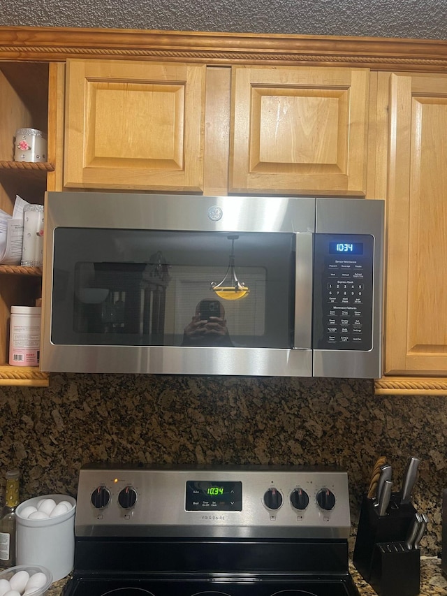 details featuring appliances with stainless steel finishes, light brown cabinetry, decorative backsplash, open shelves, and dark stone countertops