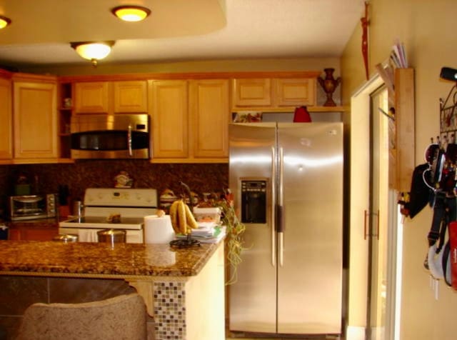 kitchen with a toaster, a breakfast bar, appliances with stainless steel finishes, backsplash, and dark stone countertops