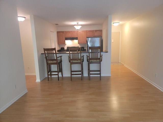 kitchen featuring kitchen peninsula, stainless steel fridge, a breakfast bar, and light hardwood / wood-style floors