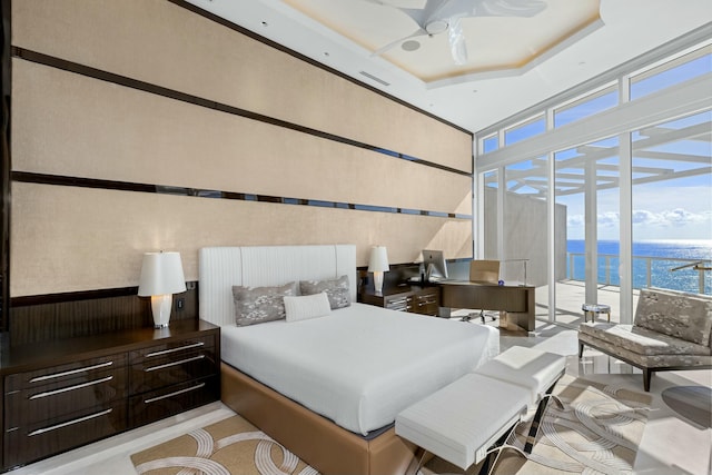 bedroom with access to outside, floor to ceiling windows, a raised ceiling, and a water view