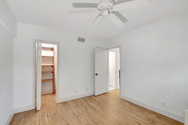 unfurnished bedroom with a walk in closet, ceiling fan, a closet, and light wood-type flooring