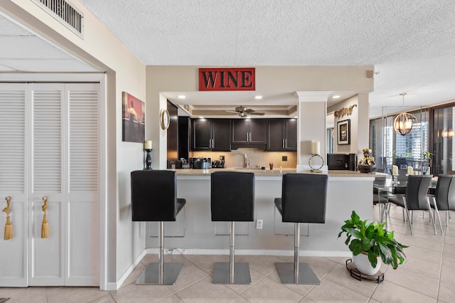 kitchen featuring kitchen peninsula, a kitchen breakfast bar, ceiling fan with notable chandelier, and light tile patterned floors