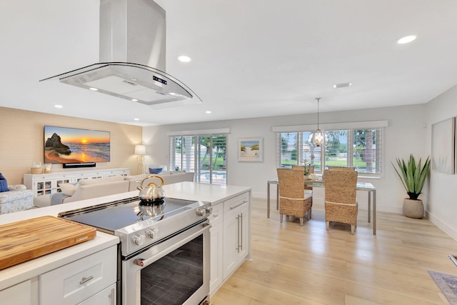 kitchen featuring island range hood, high end stove, decorative light fixtures, light hardwood / wood-style floors, and white cabinetry