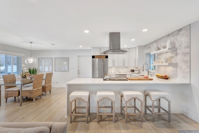 kitchen featuring island exhaust hood, stainless steel fridge, kitchen peninsula, pendant lighting, and white cabinets