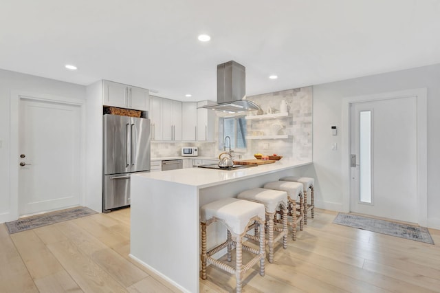 kitchen featuring kitchen peninsula, decorative backsplash, appliances with stainless steel finishes, light hardwood / wood-style floors, and white cabinetry