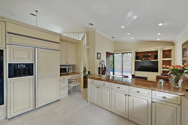 kitchen featuring lofted ceiling, dark stone counters, ornamental molding, a textured ceiling, and cream cabinetry