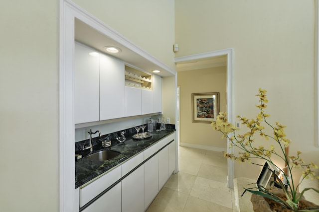 kitchen with white cabinets, dark stone countertops, light tile patterned floors, and sink