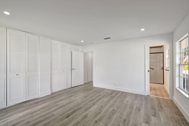 unfurnished bedroom with light hardwood / wood-style floors and multiple closets