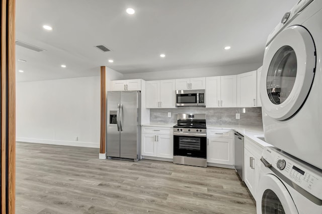 kitchen featuring appliances with stainless steel finishes, tasteful backsplash, light hardwood / wood-style flooring, stacked washer / dryer, and white cabinets