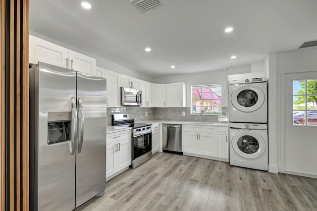 kitchen featuring white cabinets, plenty of natural light, stacked washing maching and dryer, and stainless steel appliances