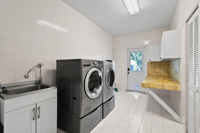 laundry area featuring cabinets, a textured ceiling, sink, light tile patterned floors, and washing machine and clothes dryer