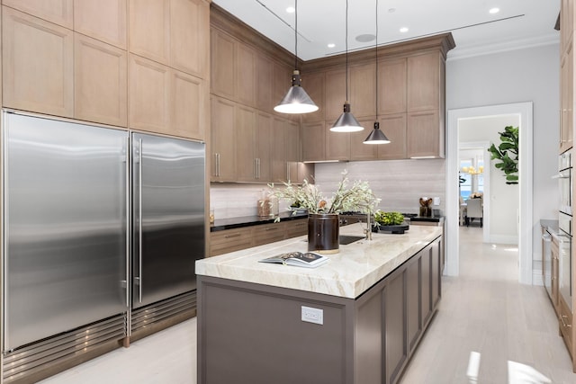 kitchen with a kitchen island with sink, stainless steel built in fridge, hanging light fixtures, ornamental molding, and tasteful backsplash