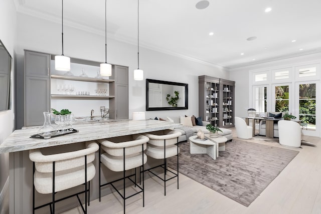 kitchen featuring gray cabinetry, light stone counters, light hardwood / wood-style flooring, decorative light fixtures, and ornamental molding