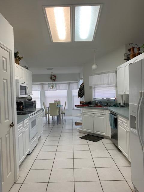 kitchen with lofted ceiling, sink, white appliances, white cabinets, and light tile patterned flooring