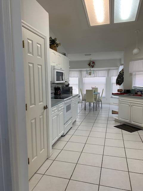 kitchen featuring light tile patterned floors, white appliances, sink, white cabinets, and vaulted ceiling