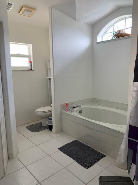 bathroom with a bathtub, plenty of natural light, tile patterned floors, and toilet