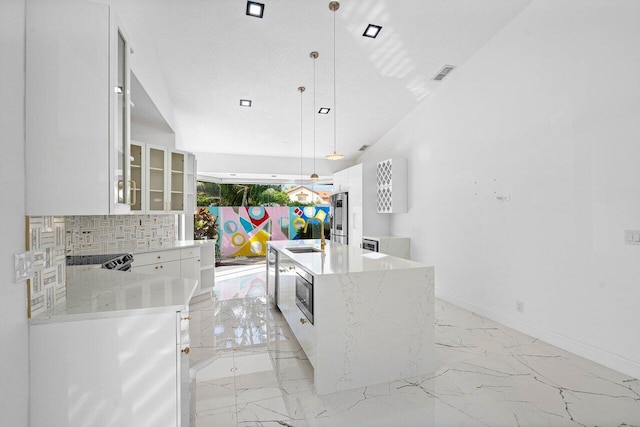 kitchen featuring hanging light fixtures, tasteful backsplash, light stone counters, an island with sink, and white cabinets