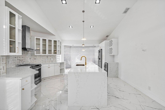 kitchen featuring backsplash, a kitchen island with sink, white cabinets, wall chimney range hood, and hanging light fixtures