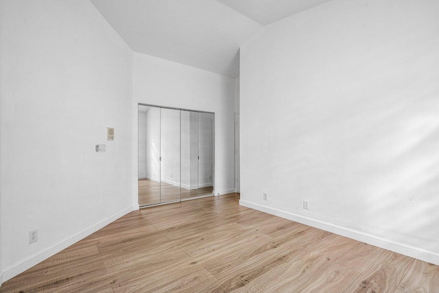 unfurnished bedroom with a closet, light hardwood / wood-style flooring, and vaulted ceiling