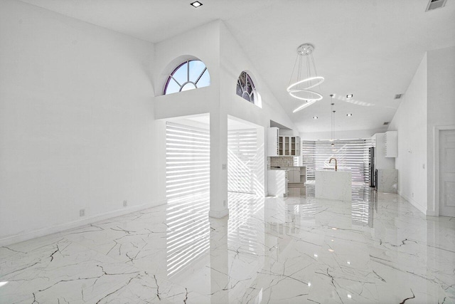 unfurnished living room with sink, high vaulted ceiling, and a chandelier