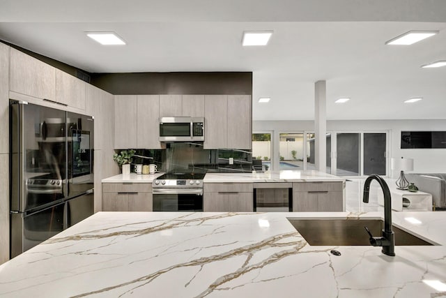 kitchen with light stone countertops, appliances with stainless steel finishes, beverage cooler, sink, and light brown cabinets